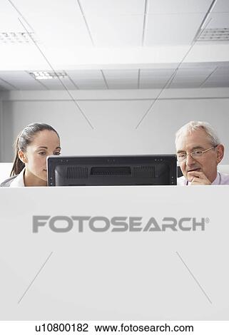 Two office workers looking at computer in office cubicle View Large Photo Image Stock Image - Two office workers looking at computer in office cubicle. Fotosearch