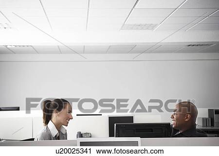 Two office workers sitting face to face in office cubicle smiling profile View Large Photo Image Stock Image - Two office workers sitting face to face in office cubicle smiling profile. Fotosearch