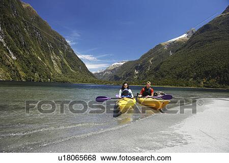Stock Photo - Two people in kayaks near shore of mountain lake. Fotosearch