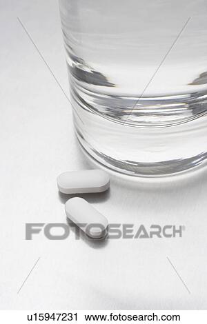 Stock Image - Two pills beside glass of water. Fotosearch
