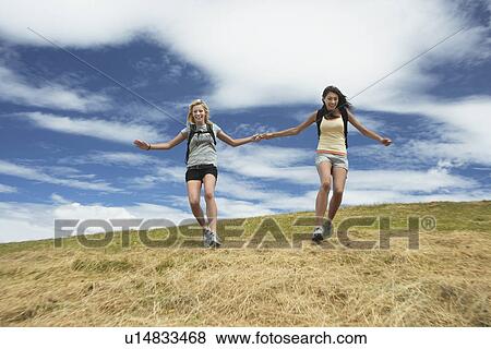 Two women holding hands skipping down hill View Large Photo Image Stock Photo - Two women holding hands skipping down hill. Fotosearch