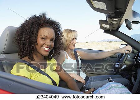 Stock Photo - Two women sitting in convertible car on desert road. Fotosearch
