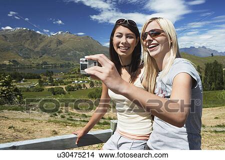 Two women taking picture against fence with mountains behind View Large Photo Image Picture - Two women taking picture against fence with mountains behind. Fotosearch