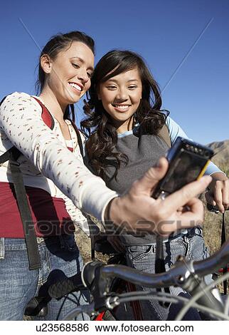 Stock Photograph - Two young women standing with bicycle photographing selves with digital camera.. Fotosearch