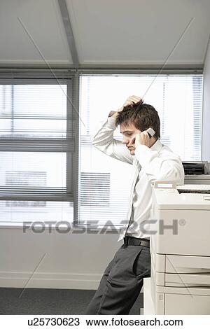 Uncertain Businessman leaning on office photcopierTalking on Cell Phone View Large Photo Image Stock Image - Uncertain Businessman leaning on office photcopierTalking on Cell Phone. Fotosearch