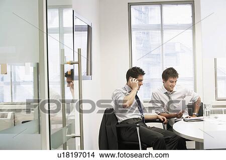 Picture - View through doorway to casual meeting between two relaxed young businessmen. Fotosearch