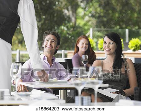 Stock Image - Waiter bringing coffee to couple at outdoor cafe. Fotosearch