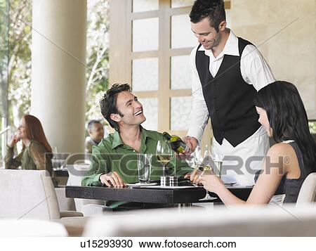 Stock Image - Waiter pouring wine for couple at outdoor restaurant. Fotosearch