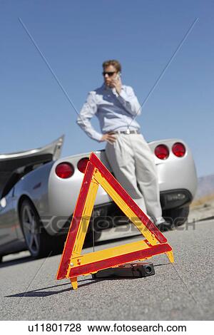 Warning triangle in front of man on cell phone by sports car View Large Photo Image Stock Photo - Warning triangle in front of man on cell phone by sports car. Fotosearch