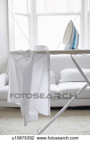 Stock Image - White shirt on ironing board in living room. Fotosearch