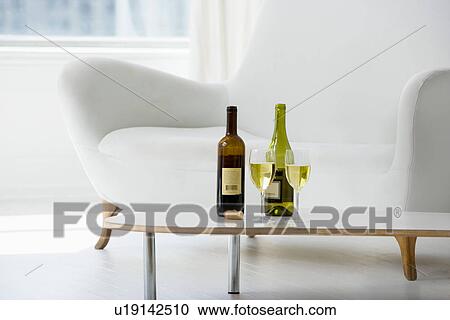 Stock Image - Wine glasses and bottles on coffee table in living room. Fotosearch