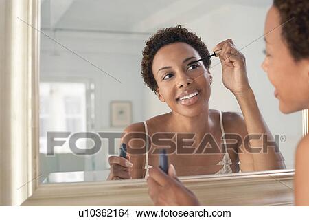 Picture - Woman applying mascara in mirror at home. Fotosearch