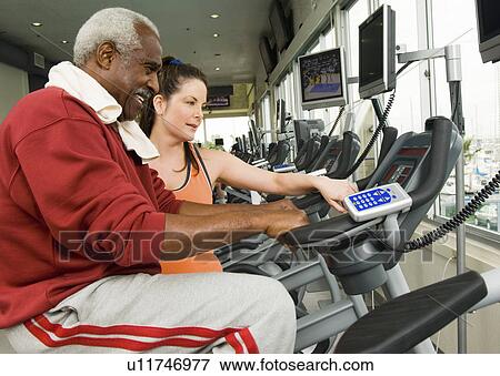 Woman assisting man on exercise bike in gymnasium View Large Photo Image Stock Photo - Woman assisting man on exercise bike in gymnasium. Fotosearch