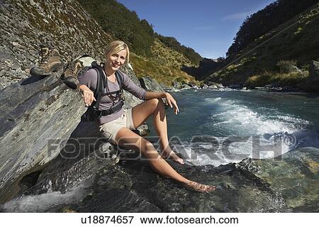 Stock Photo - Woman dipping her feet in river in forest valley. Fotosearch