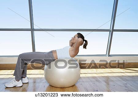 Stock Image - Woman Doing Sit-Ups on exercise ball in gym. Fotosearch