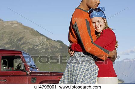 Stock Image - Woman embracing man near jeep by mountains. Fotosearch