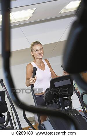 Stock Photo - Woman Exercising on Elliptical Machine in health club. Fotosearch