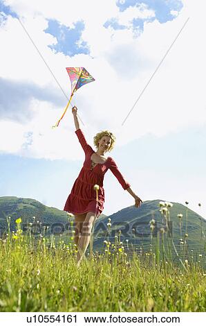 Stock Image - Woman Flying Kite in mountain field front view. Fotosearch