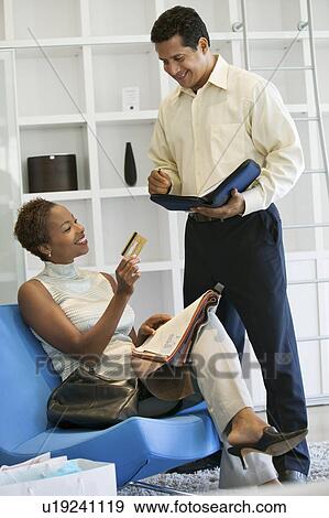 Stock Photo - Woman giving partner Credit Card in furniture store. Fotosearch
