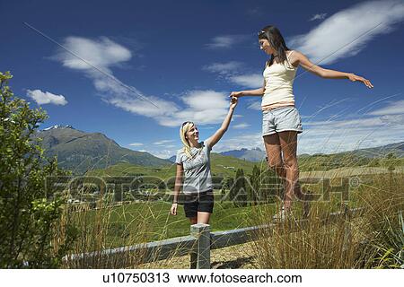 Stock Image - Woman helping another woman walk along fence in countryside. Fotosearch