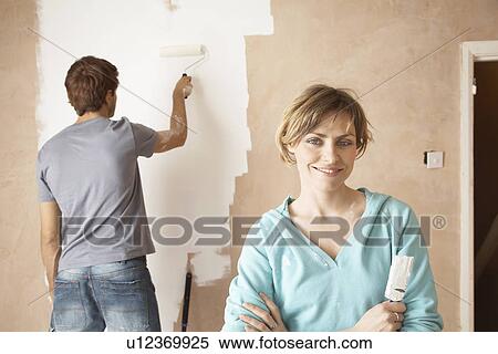 Stock Photography - Woman holding paint brush next to man painting interior wall. Fotosearch