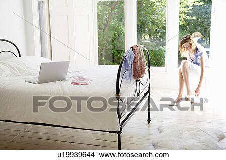 Picture - Woman in bedroom putting on shoes. Fotosearch