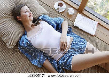 Woman in pajamas lying on couch with coffee and magazine on window sill View Large Photo Image Stock Image - Woman in pajamas lying on couch with coffee and magazine on window sill. Fotosearch