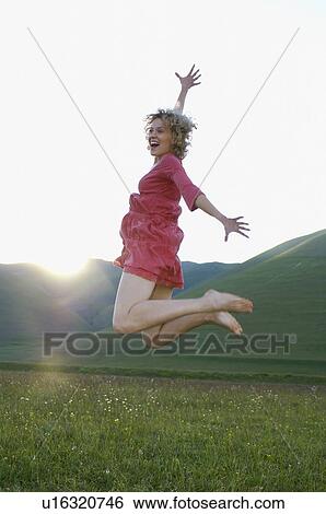 Stock Photograph - Woman jumping for joy in mountain meadow side view. Fotosearch