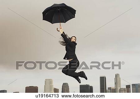 Woman jumping with umbrella mid-air above city View Large Photo Image Stock Image - Woman jumping with umbrella mid-air above city. Fotosearch