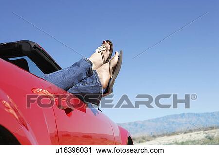 Woman lying in red convertible on desert road low section View Large Photo Image Stock Image - Woman lying in red convertible on desert road low section. Fotosearch