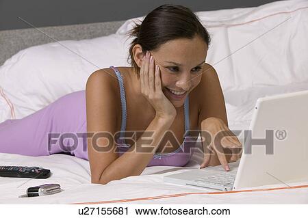 Woman lying on bed using laptop View Large Photo Image Stock Image - Woman lying on bed using laptop. Fotosearch