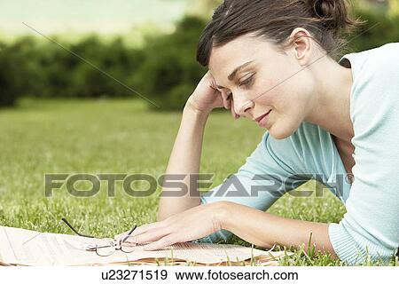 Stock Photo - Woman lying on grass reading newspaper.. Fotosearch