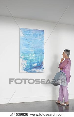 Woman observing painting in art gallery View Large Photo Image Stock Photograph - Woman observing painting in art gallery. Fotosearch