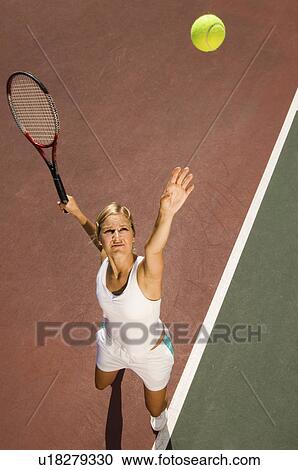Stock Image - Woman on tennis court Serving Tennis Ball elevated view. Fotosearch