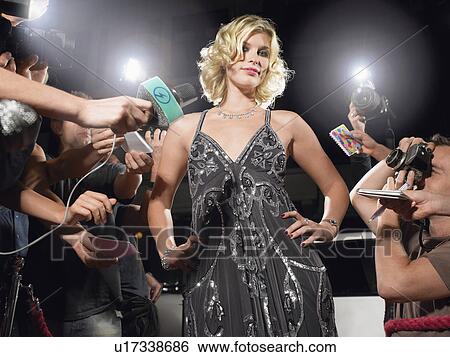 Stock Photograph - Woman posing on red carpet being photographed by paparazzi. Fotosearch