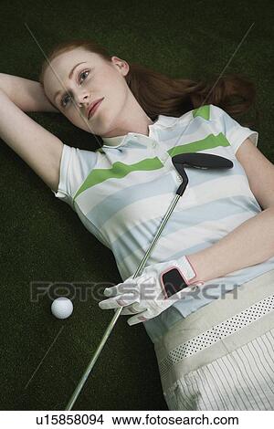 Picture - Woman reclining on floor holding golf club portrait elevated view. Fotosearch