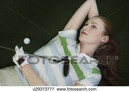 Stock Photo - Woman reclining on floor holding golf club portrait elevated view. Fotosearch