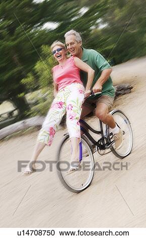 Stock Image - Woman riding on handlebars of mans bicycle. Fotosearch