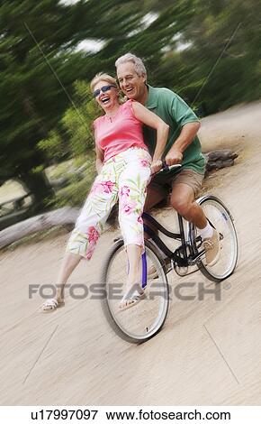 Stock Photo - Woman riding on handlebars of mans bicycle. Fotosearch