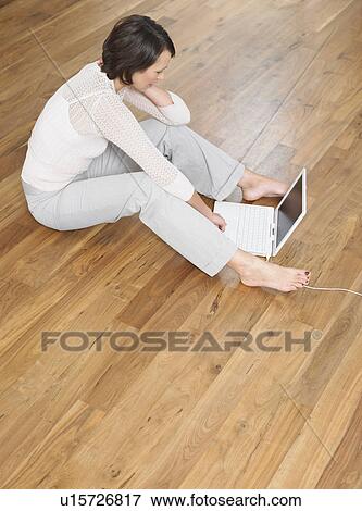 Stock Photo - Woman sat on wood panel floor using laptop. Fotosearch