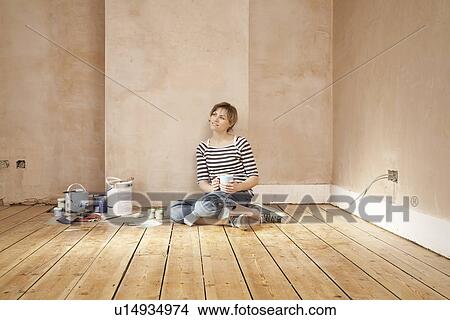 Woman sitting on floor of unrenovated room holding coffee mug View Large Photo Image Picture - Woman sitting on floor of unrenovated room holding coffee mug. Fotosearch