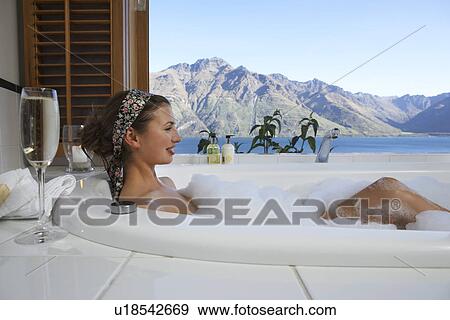 Woman taking a bubble bath with champagne with mountain lake outside window View Large Photo Image Stock Photo - Woman taking a bubble bath with champagne with mountain lake outside window. Fotosearch