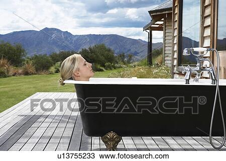 Stock Image - Woman taking bath on porch by mountains. Fotosearch