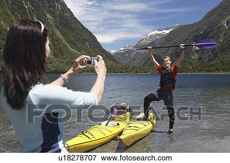 Woman taking picture of man hoisting oar of kayak over head on shore of mountain lake View Large Photo Image Stock Photo - Woman taking picture of man hoisting oar of kayak over head on shore of mountain lake. Fotosearch