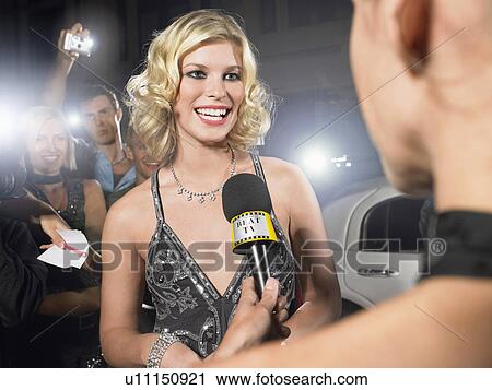 Stock Image - Woman talking into microphone on red carpet. Fotosearch