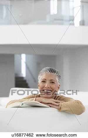 Stock Image - Woman with book on sofa smiling portrait. Fotosearch