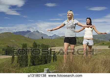 Women balancing on fence in field with mountains behind View Large Photo Image Stock Photo - Women balancing on fence in field with mountains behind. Fotosearch
