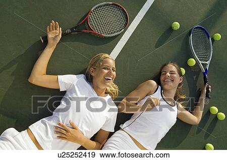 Stock Photo - Women Fatigued and Laughing lying on tennis court After Tennis Match view from above. Fotosearch