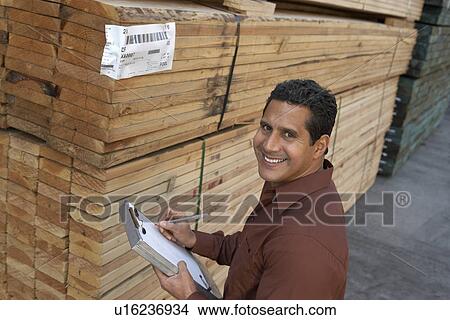 Worker taking notes on clipboard by stack of wood in warehouse elevated view View Large Photo Image Picture - Worker taking notes on clipboard by stack of wood in warehouse elevated view. Fotosearch
