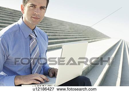 Young businessman sitting on steps using laptop portrait. View Large Photo Image Stock Photo - Young businessman sitting on steps using laptop portrait.. Fotosearch